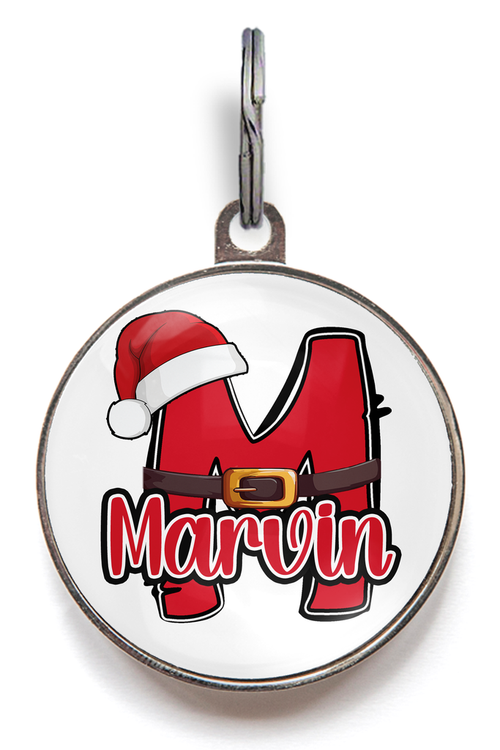 Santa Monogram Dog Tag. Featuring an alphabet letter in red, dressed with a Santa hat and belt. Pet's name overlays this. Example shown is the letter M with the name Marvin. 