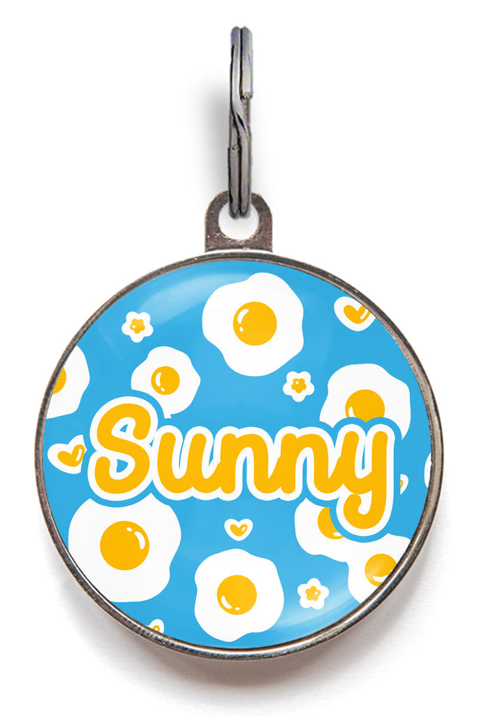Fried egg pet name tag with blue background, white and yellow egg pattern, and “Sunny” text – customisable for dogs or cats.